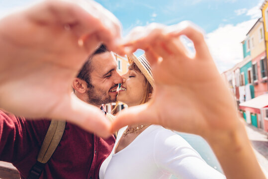 Close up of young couple in love making heart shape with hands outdoor at vacation. 