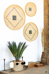 Wooden shelf or shelf with wicker baskets for storage in the kitchen or living room. Wooden tabletop with decorative coasters, candles and living plants. 