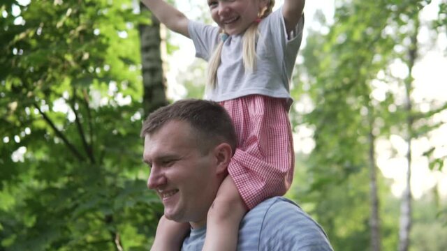 A Pretty little girl sits on her dad's shoulders during a summer walk. Beautiful sunset light