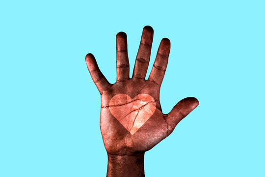Open palm of a African American man with a heart drawn asking for the stop of racism. Black hand isolated on a blue background.