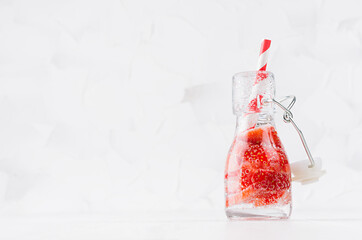 Fresh strawberry lemonade with sliced berry, soda water, straw in transparent yoke bottle on soft light white wood table, copy space.