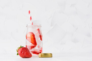 Summer homemade drink - infused strawberry water with sliced berry, ice cubes, soda, cap, straw in soft light white interior, copy space.