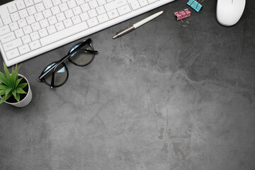 Flat lay business office concept on vintage cement table desk background with white keyboard computer and eyeglasses, coffee cup and green plant, mouse and paper clip, Top view with copy space
