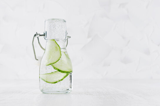 Fresh summer cocktail with green cucumber, soda in yoke bottle on elegant soft light white wooden board and plaster wall.