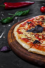 Perfect pizza margarita with tomato slices, basil on a dark background.