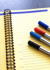 Open diary, planner and a set of markers on a close-up table.