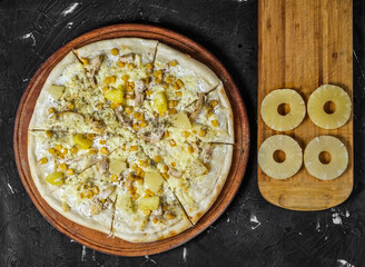 Isolated Pizza with chicken and pineapple on a wooden board, and on a dark background