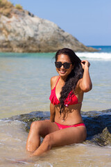 Beautiful tanned woman in a red bikini swimsuit on the beach.