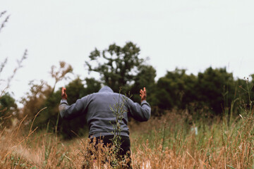 Naklejka na ściany i meble young man praying in the field with hands lifted