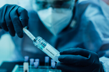 A biologist with gloves, mask, and glasses loads a syringe with a dose of Dexamethasone (covid-19 coronavirus cure)