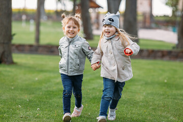 Two happy cute girls running in the park holding hands