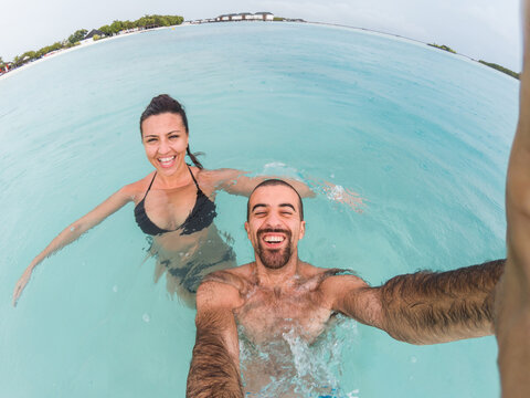 Happy couple taking a candid selfie at Maldives resort and enjoying seaside under the rain - Smiling and laughing young people at summer destination - Tropical beach vacation at ocean paradise