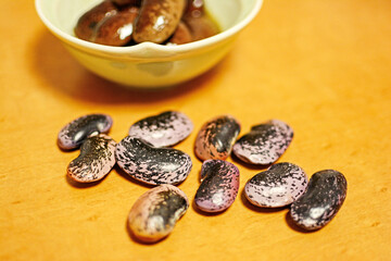 乾燥した数粒の紫花豆と、白い陶器の器に盛り付けられた丸々と膨らんだ信州名産のインゲンマメ属の大きな紫花豆の煮物。The dried scarlet runner beans and  the cooked dish of some scarlet runner beans 旅行、旅先、シルバーウィーク、紅葉。