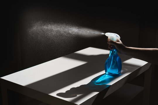 Crop anonymous person pushing dispenser mechanism and directing white cleaner flow on black wall while bottle being placed on white table with shadows