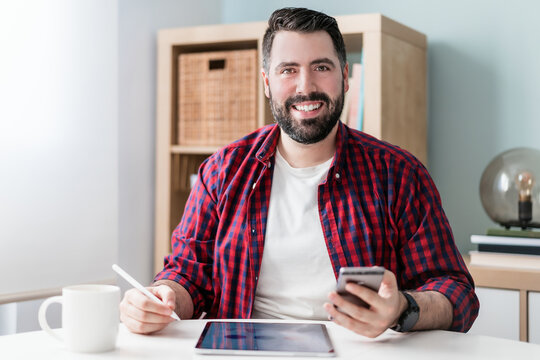 A young man is writing on a tablet. The man is working from home. The entrepreneur is holding a phone