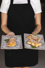 Woman with apron holding syrniki and pancakes roll with with powdered sugar or confectioner sugar.