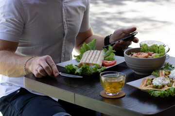 Man eating lunch, breakfast or brunch outside the cafe, salad, tea, wrap, waffles, pouched eggs