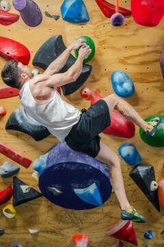 From bellow unrecognizable strong male athlete in sportswear climbing on colorful wall during workout in modern climbing center
