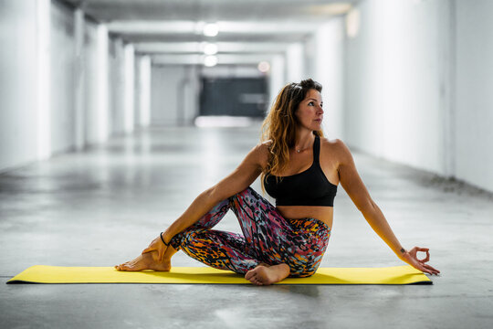 Side view of concentrated young female in active wear doing Half Spinal Twist asana during yoga session in modern light garage