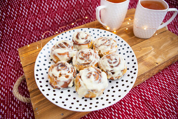 Two cups of black tea stand on a wooden tray. Fresh and fragrant cinnamon rolls close up lie on a plate with polka dots, beautiful morning. Close-up. Romantic morning. View from above