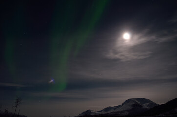 Fototapeta na wymiar aurora borealis, northern light over snowy winter landscape with mountain and full moon at night