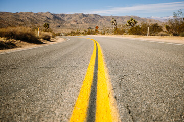 Straight asphalt road going through sandy terrain with dry grass and mountains on background of cloudy sky on heat day in California