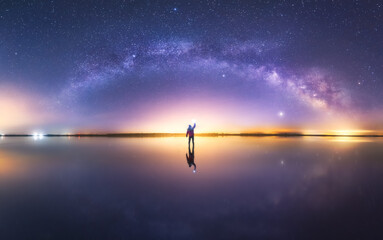 Silhouette of anonymous man standing on reflection surface of water and reaching out to starry colorful night sky with milky way