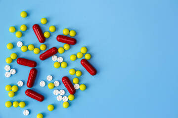 A handful of multicolored tablets of various shapes are scattered randomly on a blue background. Medical concept, treatment of diseases and viruses, healthcare, pharmacy. Copy the space for the text