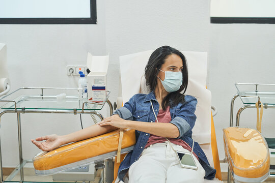 female donor with patch on hand sitting in medical chair after blood transfusion procedure
