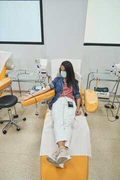 woman in protective mask sitting in medical armchair during blood transfusion procedure in contemporary hospital