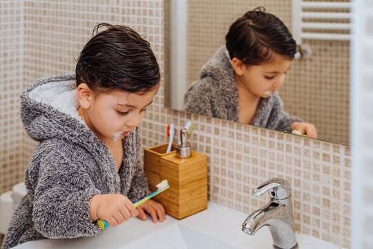 Adorable child wearing cozy bathrobe standing in bathroom with toothbrush