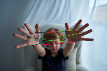 Closeup of hands of boy playing cats cradle game and demonstrating basic figure made with colorful string while spending free time at home