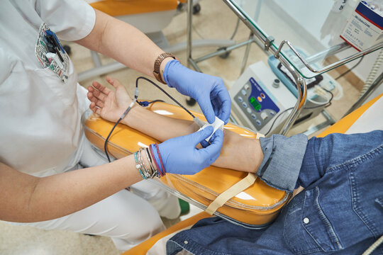 Crop female medical specialist in latex gloves performing injection with syringe to anonymous patient during procedure of blood transfusion in hospital