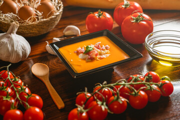 Receta típica española de salmorejo cordobés en un plato cuadrado y con algunos ingredientes al rededor.