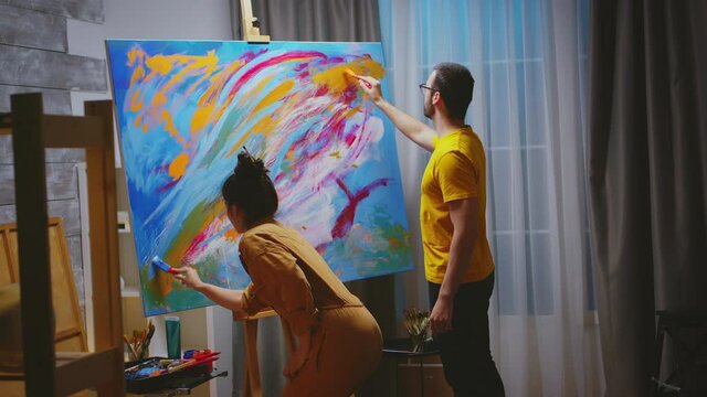Man and woman painters working together in art studio on large canvas. Modern artwork paint on canvas, creative, contemporary and successful fine art artist drawing masterpiece