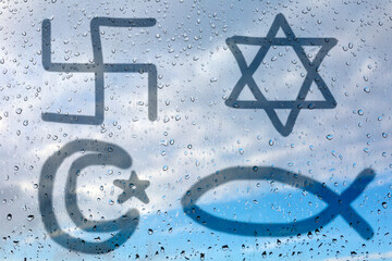 Figure of the four religious symbols - Christianity, Judaism, Hinduism and Islam on wet glass. Glass window with raindrops against the sky. The concept of the basic religions of the world - 358591105