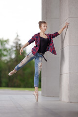 Girl ballerina in jeans, a plaid shirt and pointe shoes dancing in the city on the street © Tatiana
