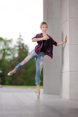 Girl ballerina in jeans, a plaid shirt and pointe shoes dancing in the city on the street © Tatiana