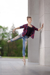 Girl ballerina in jeans, a plaid shirt and pointe shoes dancing in the city on the street © Tatiana