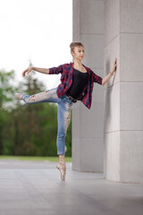 Girl ballerina in jeans, a plaid shirt and pointe shoes dancing in the city on the street © Tatiana