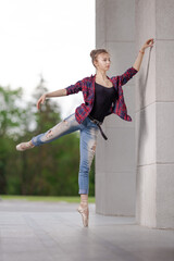 Girl ballerina in jeans, a plaid shirt and pointe shoes dancing in the city on the street © Tatiana