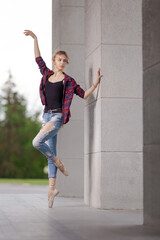 Girl ballerina in jeans, a plaid shirt and pointe shoes dancing in the city on the street © Tatiana