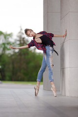 Girl ballerina in jeans, a plaid shirt and pointe shoes dancing in the city on the street © Tatiana
