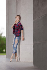Girl ballerina in jeans, a plaid shirt and pointe shoes dancing in the city on the street © Tatiana