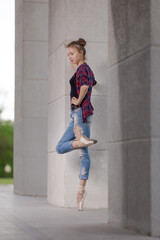 Girl ballerina in jeans, a plaid shirt and pointe shoes dancing in the city on the street © Tatiana