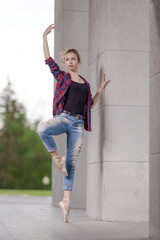 Girl ballerina in jeans, a plaid shirt and pointe shoes dancing in the city on the street © Tatiana