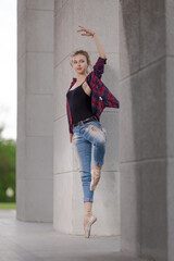 Girl ballerina in jeans, a plaid shirt and pointe shoes dancing in the city on the street © Tatiana