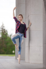 Girl ballerina in jeans, a plaid shirt and pointe shoes dancing in the city on the street © Tatiana