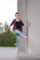 Girl ballerina in jeans, a plaid shirt and pointe shoes dancing in the city on the street © Tatiana