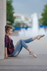 Girl ballerina in jeans, a plaid shirt and pointe shoes dancing in the city on the street © Tatiana